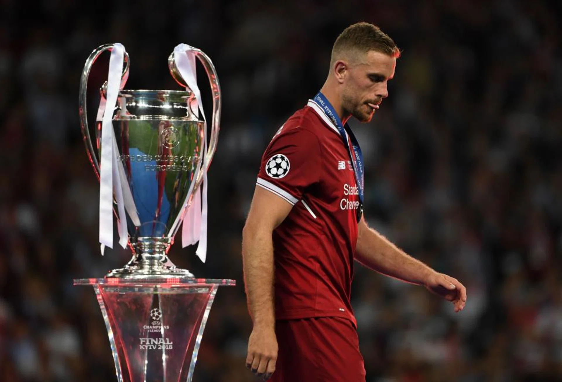 Liverpool skipper Jordan Henderson walking past the Champions League trophy.