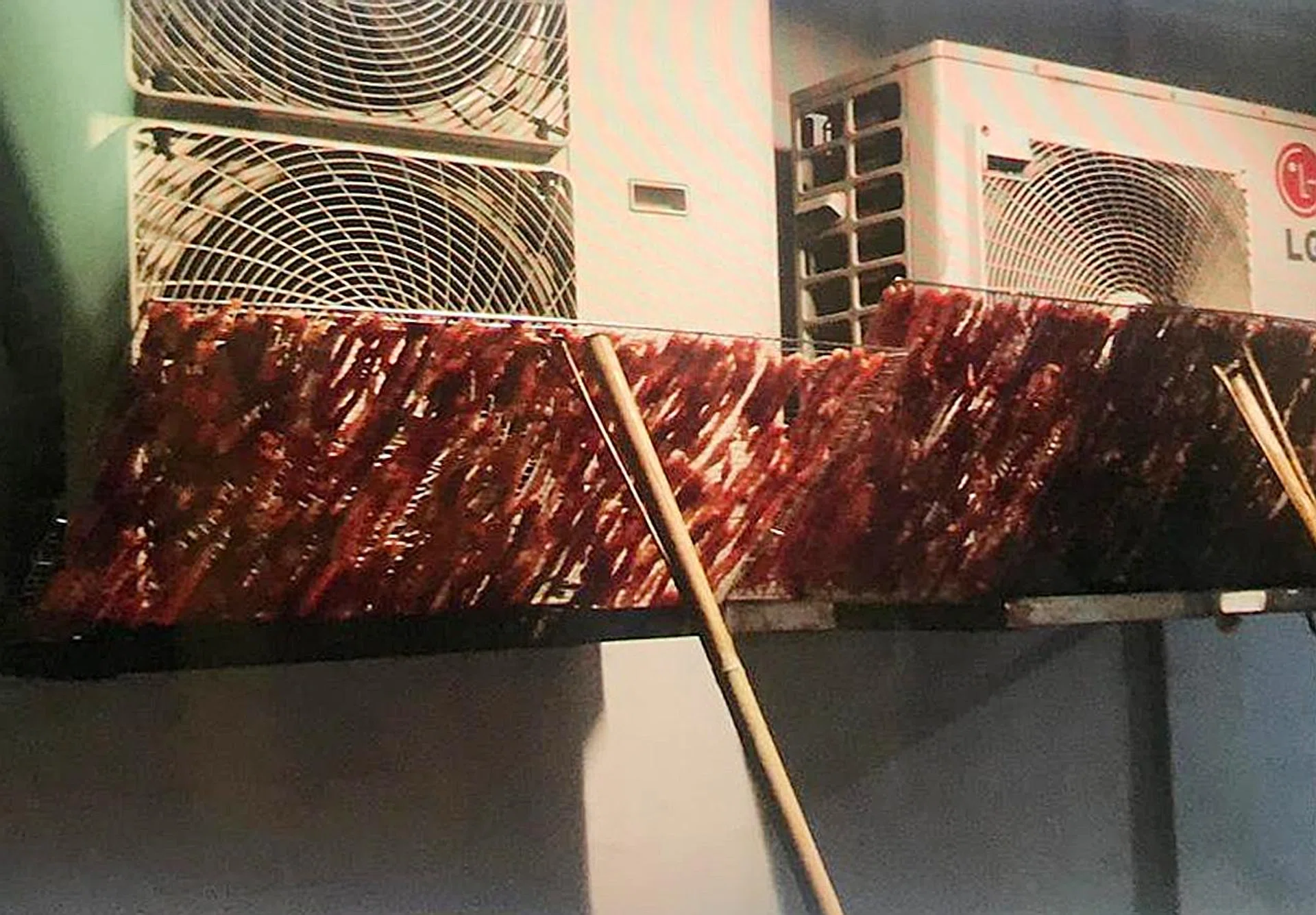Racks of raw meat being hung to dry outside dusty air-conditioner compressor vents at a HDB block in Beach Road. 