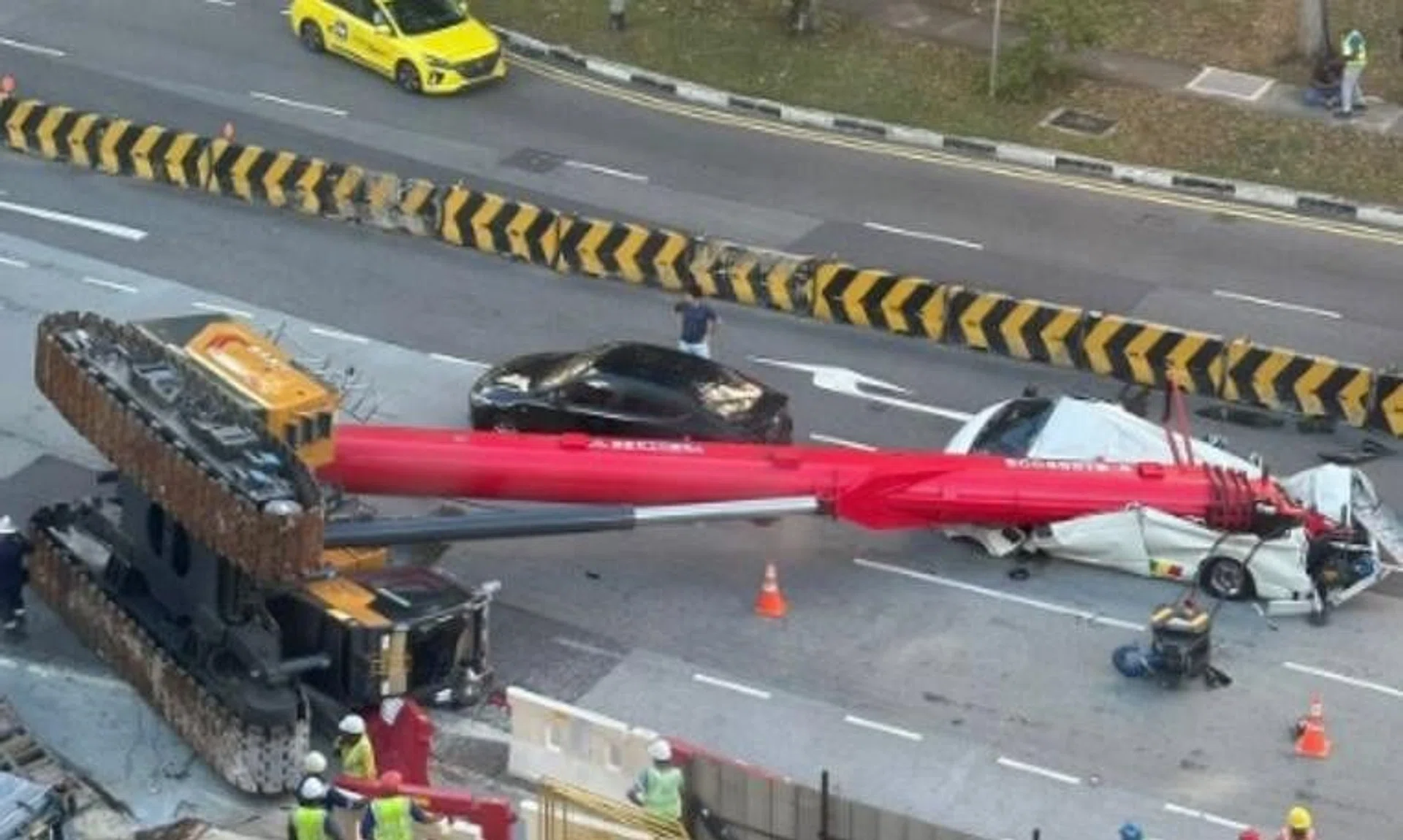 The fallen crane can be seen lying on its side, with its boom stretching across the width of the road and resting on a white van.