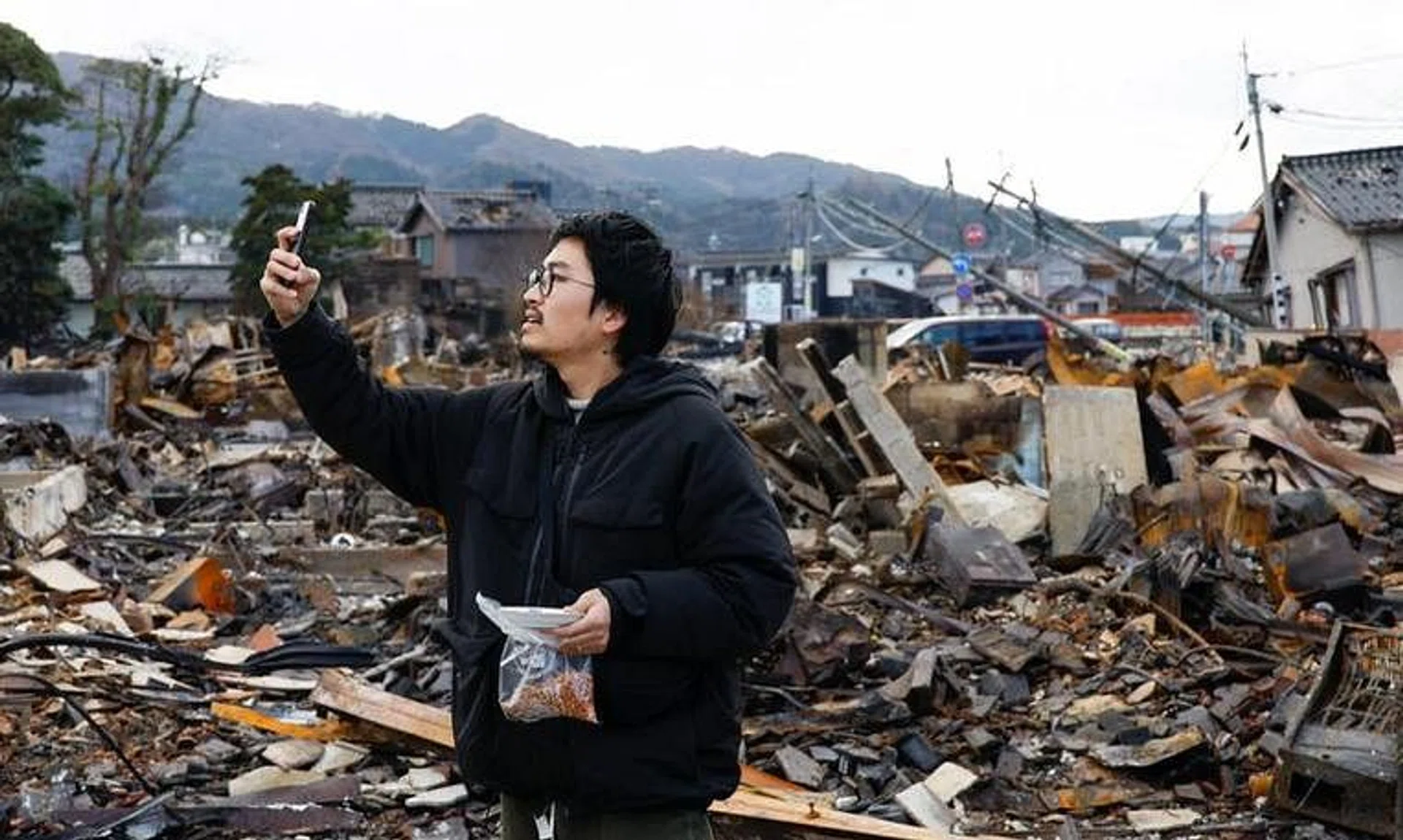 Japanese lacquer artist Kohei Kirimoto takes photos, while searching for his cats, next to an \"Asaichi\" morning market which burnt down in a quake-triggered fire, in Wajima, Japan, January 4, 2024. REUTERS/Kim Kyung-Hoon