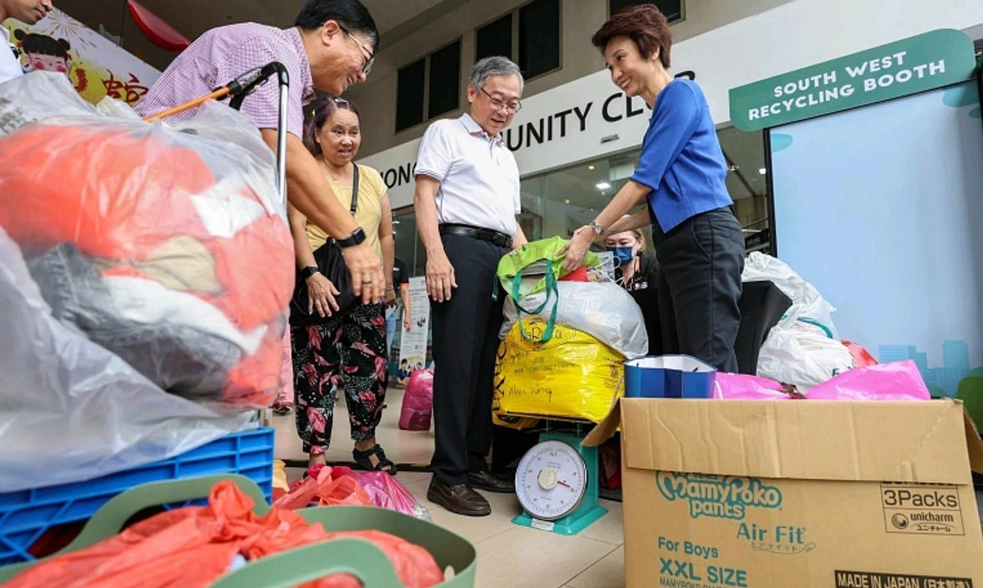 DPM Gan Kim Yong (centre) and South West District Mayor Low Yen Ling (right) helping Madam Chee Wot Yeen (in yellow) weigh the old clothes and newspapers that she brought to Keat Hong CC.