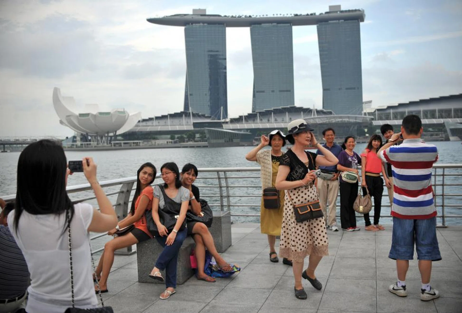 Tourists taking photos at the Merlion Park with Marina Bay Sands in the background.