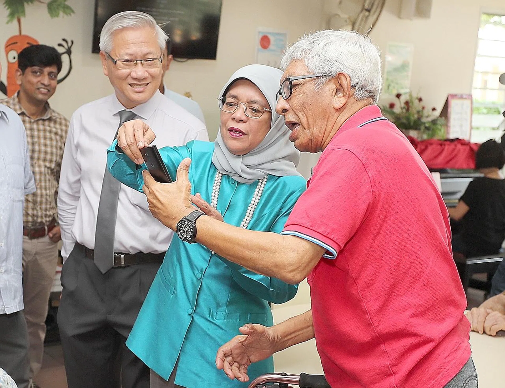 Mr Arvind Sharma takes a selfie with President Halimah Yacob as St John's Home chairman Woon Wee Yim looks on. 