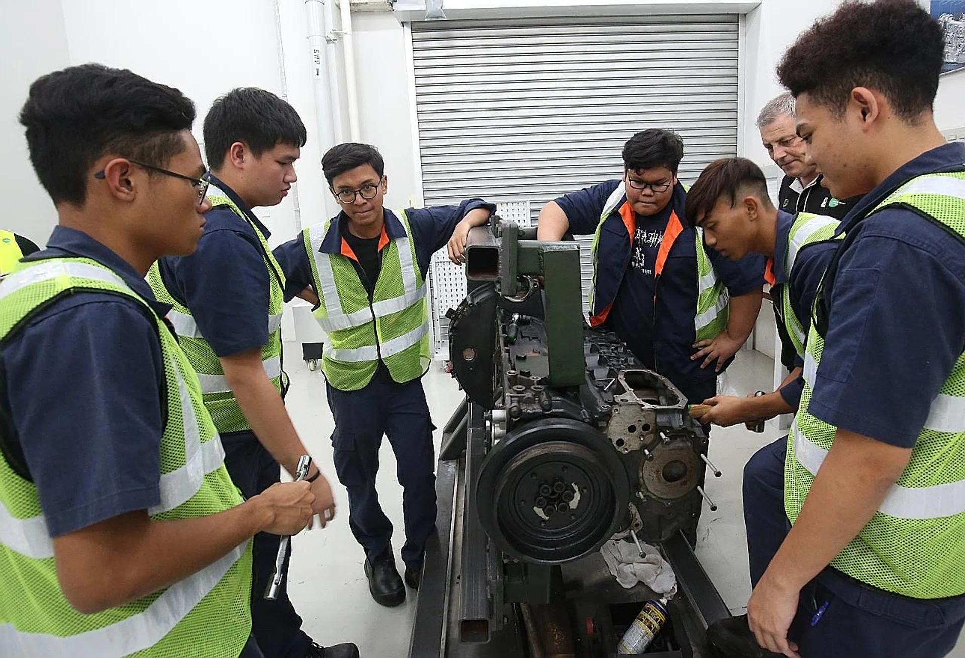 Students working on a bus component under the supervision of a Tower Transit Singapore engineer. 