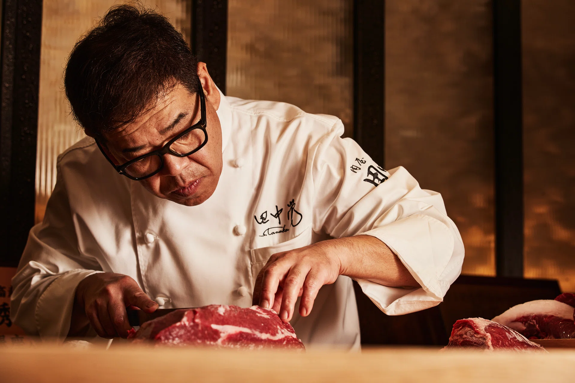 A man in chefs garb cuts a thin slice of beef.