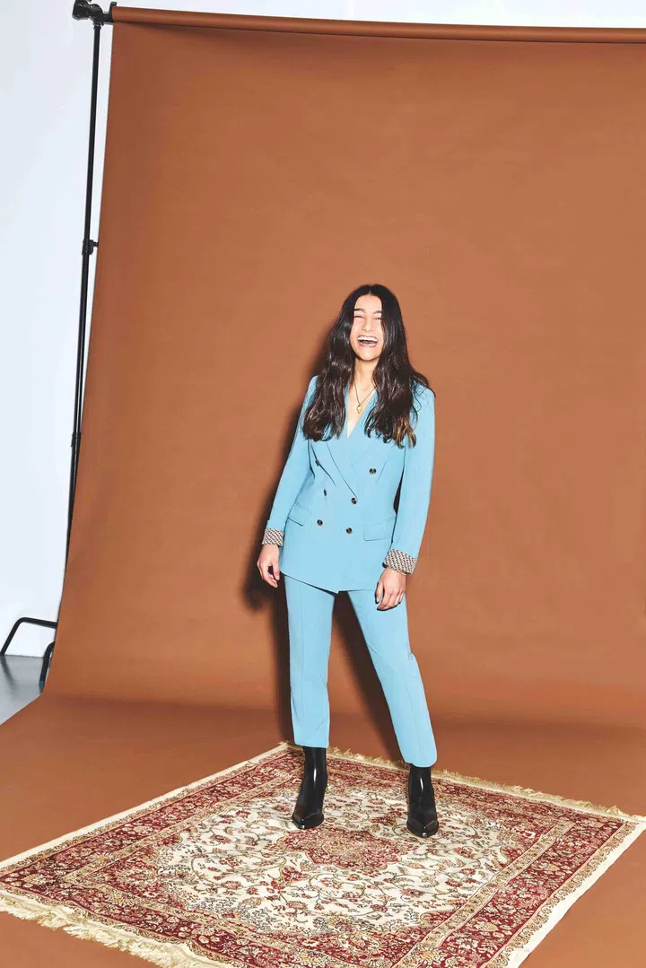 Carmen Calisto is wearing a green polyester double breasted suit from Diane von Furstenberg and black leather lean boots from Bottega Veneta.