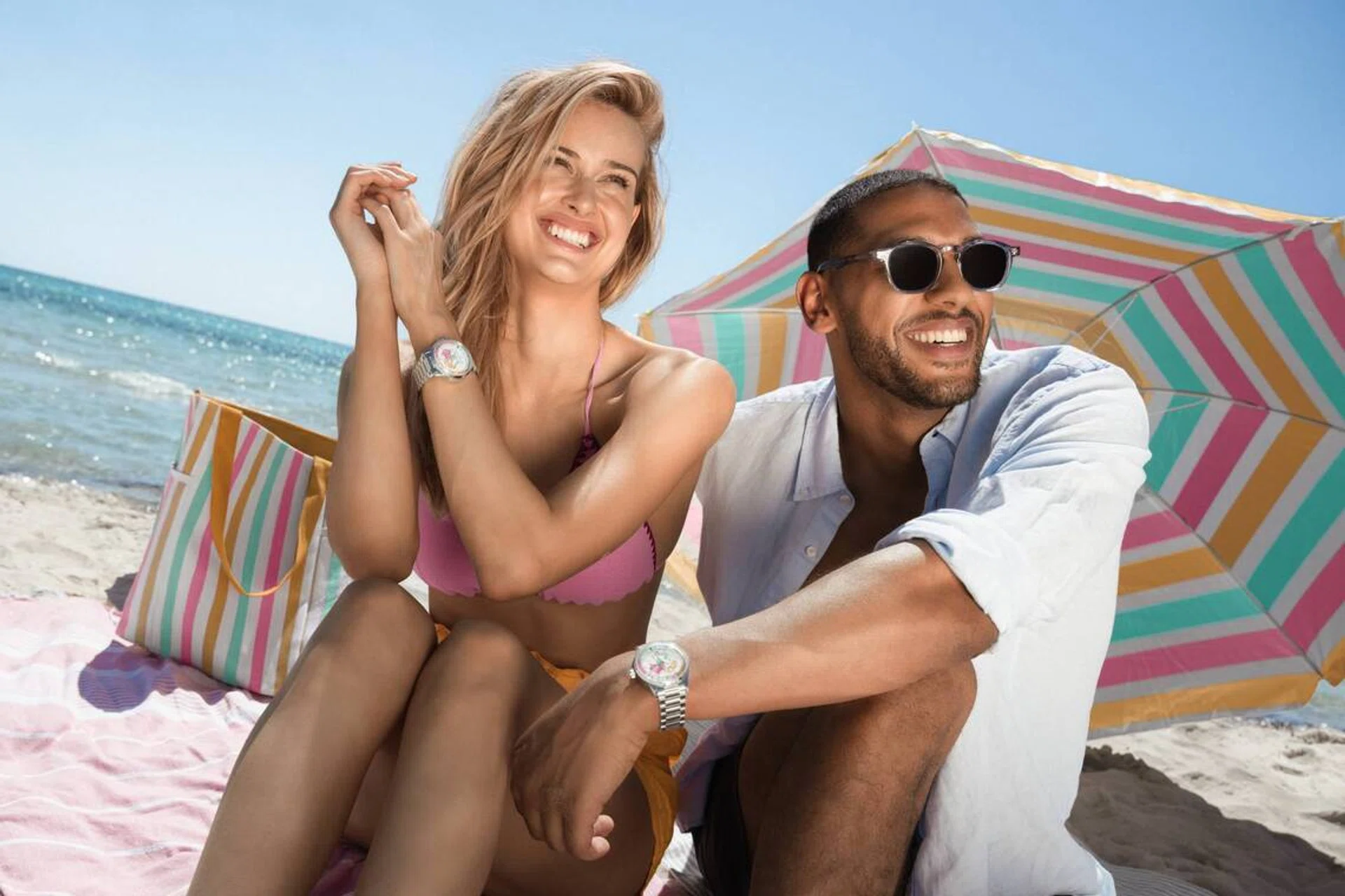 Two models on Ayada Maldives’ beach wearing Norqain Freedom GMT Enjoy Life “Holiday” Limited Edition watches, with turquoise waters and white sand in the background.