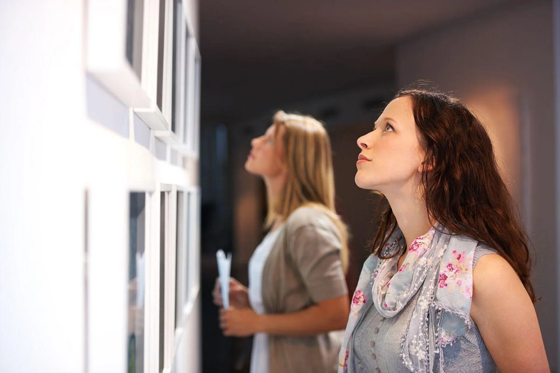 Two female friends viewing paintings while attending an exhibition