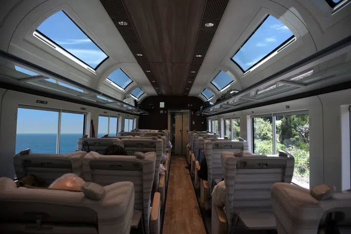 Interior of the Saphir Odoriko luxury sightseeing train in Japan, featuring elegant wood-panelled cabins, spacious seating, large panoramic windows and refined interiors designed for scenic journeys between Tokyo and the Izu Peninsula.