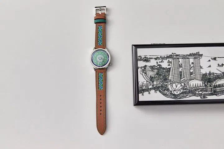 The Feynman Coalesce "Peacock" watch next to one of the two boxes that came with it. This one features an illustration by Glenn Phua, a student of Pathlight School.