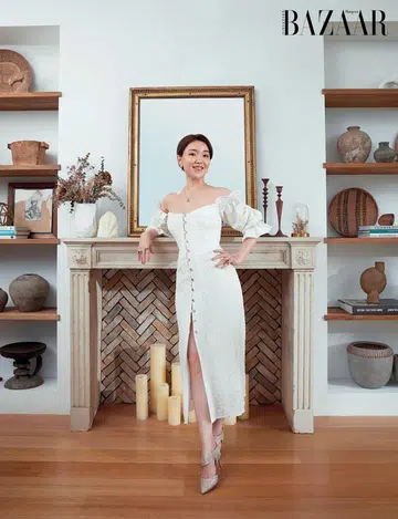 Vivienne Shen, wearing her own Cult Gaia dress, vintage earrings, Bvlgari necklace, vintage rings and Nicholas Kirkwood heels, in front of her 18th‑century‑inspired faux fireplace.