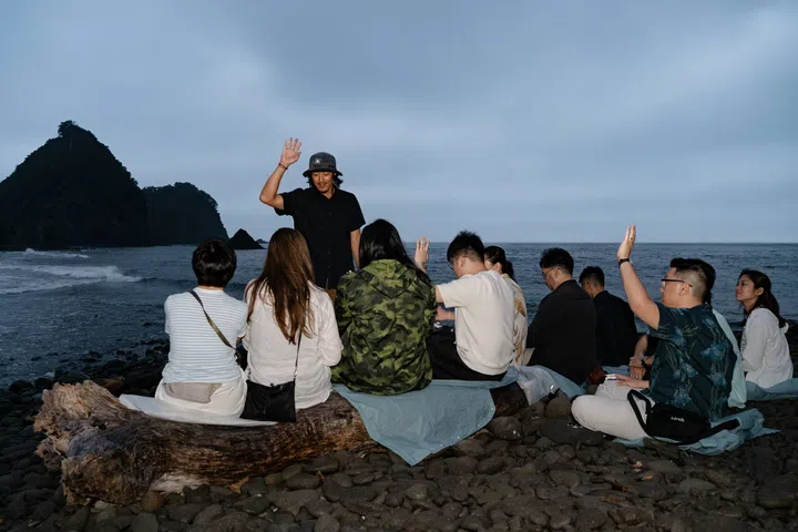 Award-winning freediving photographer Kohei Ueno leading a breathing exercise on Sebama Coast in western Izu Peninsula, with participants seated on the shoreline overlooking the Pacific Ocean as part of the Grand Seiko Ushio Journey.