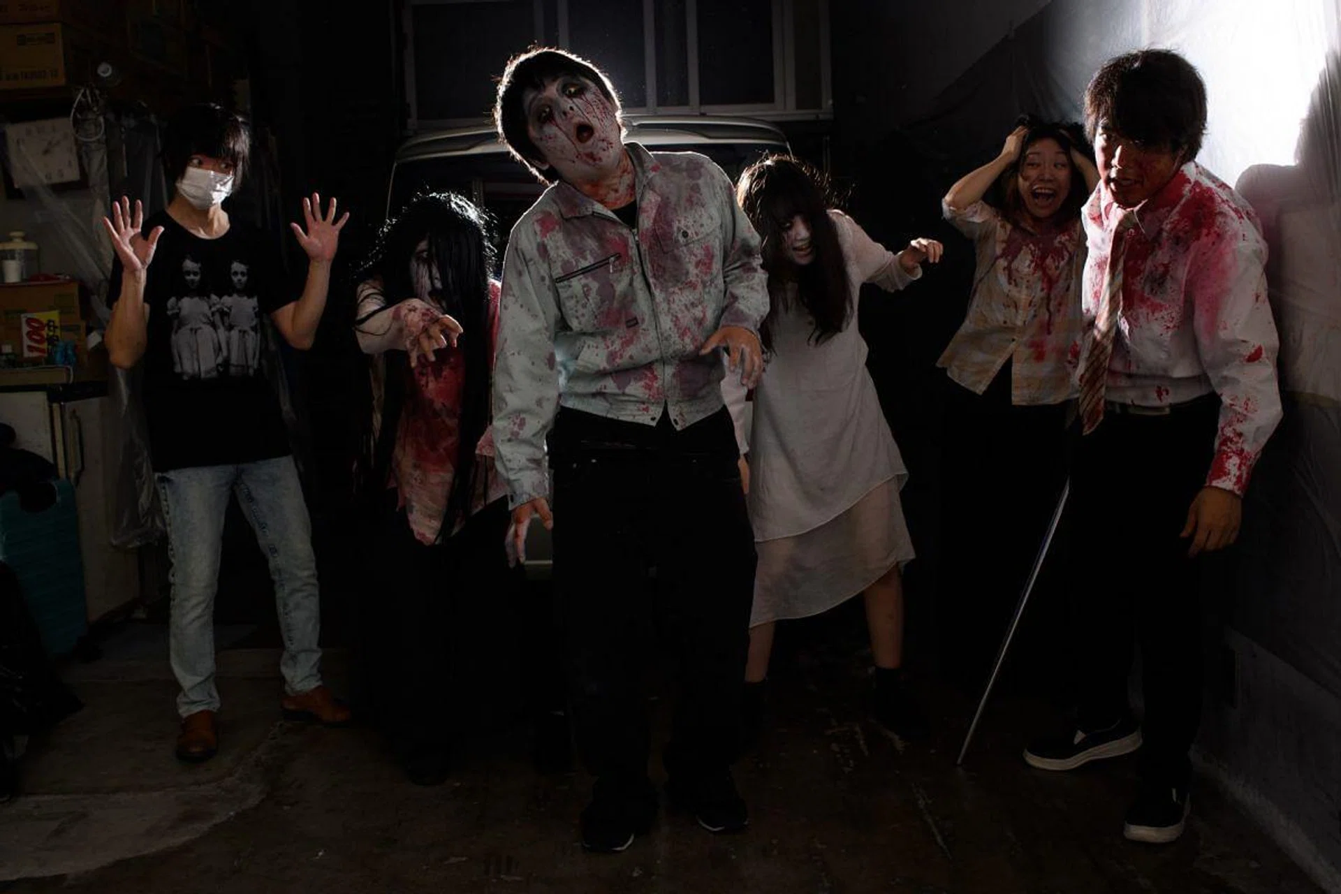 This picture taken on June 15, 2020 shows a group photo of (L-R) sound and lights engineer Daichi Ono, 33, Ayaka Imaide, 34, Kenta Iwana, 25, Haruna Suzuki, 20, Asami Takeuchi, 33, Kota Hanegawa, 28, posing before an interview in a drive-in haunted house in Tokyo. - A car horn beeps and the horror begins: a bloody murder and rampaging zombies. But this drive-in haunted house in Japan protects against the most terrifying enemy of all -- coronavirus. Inside a car, guests can scream as loudly as they like, with no mask required, as hideous creatures daubed in blood swarm towards them. (Photo by Philip FONG / AFP) / TO GO WITH AFP STORY JAPAN-ENTERTAINMENT-HEALTH-VIRUS-HORROR,FOCUS BY HARUMI OZAWA