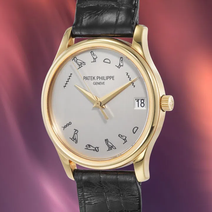 Front view of the Patek Philippe Calatrava Ref. 3998J-013 in 18k yellow gold, featuring a white dial with black Egyptian hieroglyphs in place of conventional hour markers, a small seconds sub-dial at 6 o’clock, slim gold bezel, and black leather strap.