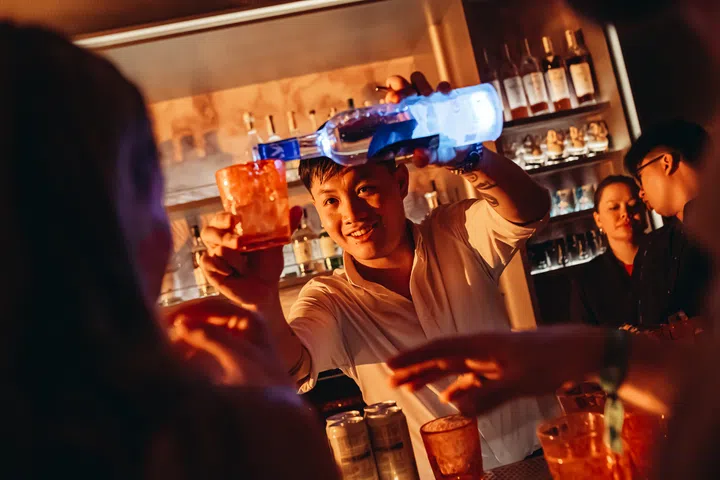 A man behind the bar pours alcohol into a cup.