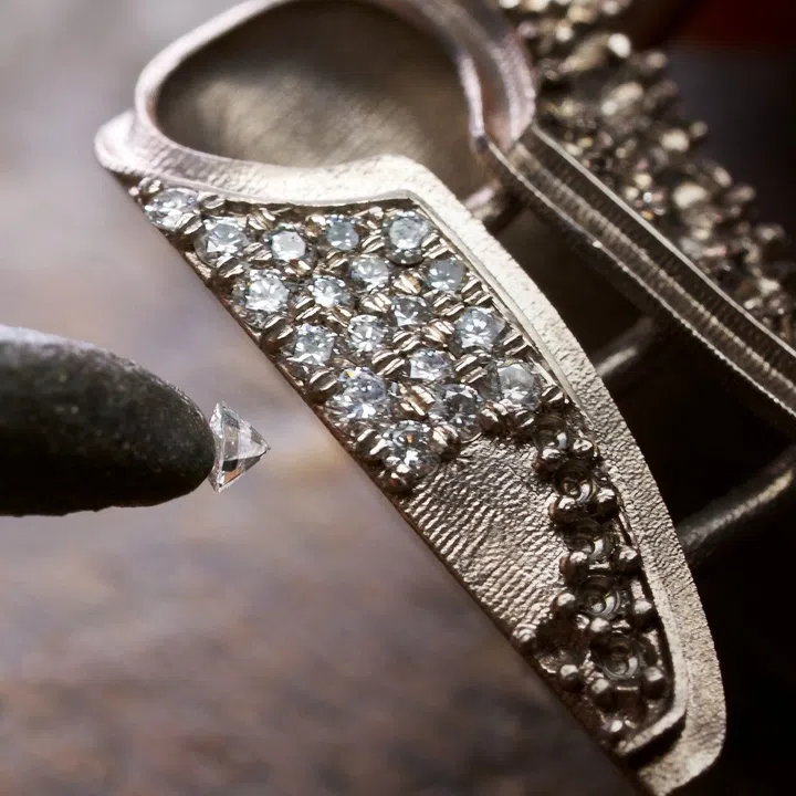 Close-up of artisans setting diamonds into the tweed-inspired jacket of the Coco Chanel queen figurine using Chanel’s tweed-setting technique.