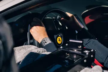 Image of a car driver wearing the Richard Mille RM UP-01 Ferrari, positioned next to a Ferrari insignia.