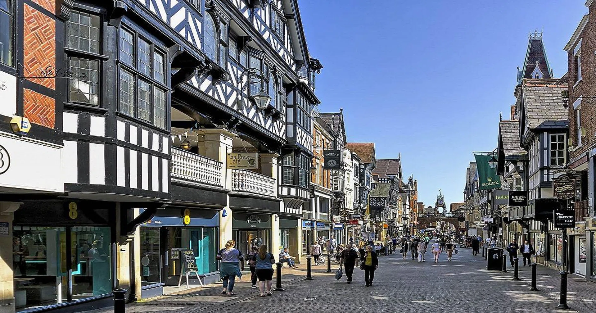 View along the main street in the centre of Chester, Cheshire, UK.  Shops can be seen on either side of the road and people can be seen walking and sitting on benches.