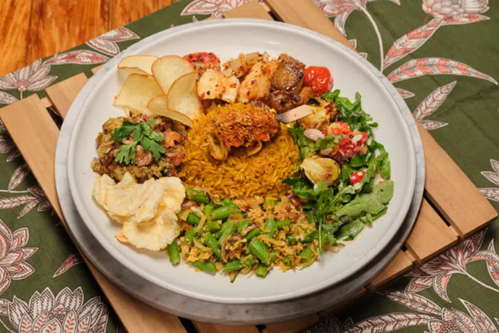 A plate full of various dishes is put on top of a wooden-slated mat.