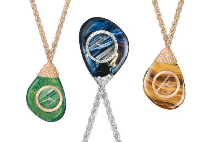 Three Piaget Swinging Pebbles sautoir watches suspended from hand-crafted gold chains, each carved from ornamental stone including tiger’s eye, verdite and pietersite, with asymmetrical pebble-shaped cases that transform the timepieces into wearable jewellery sculptures.