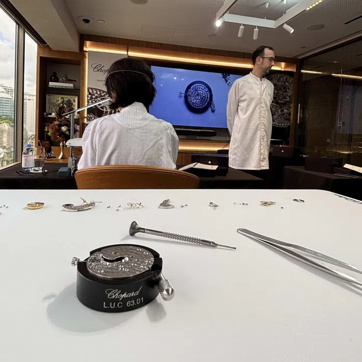 Participants seated at individual workbenches during the Chopard watchmaking masterclass follow a close-up demonstration of dismantling and assembling the L.U.C Calibre 63.03-C movement projected onto a screen, with two instructors circulating around the room to provide one-to-one guidance and assistance.