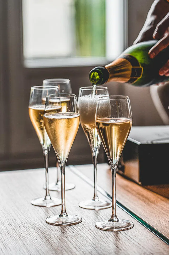 One hand is pouring champagne into four glasses