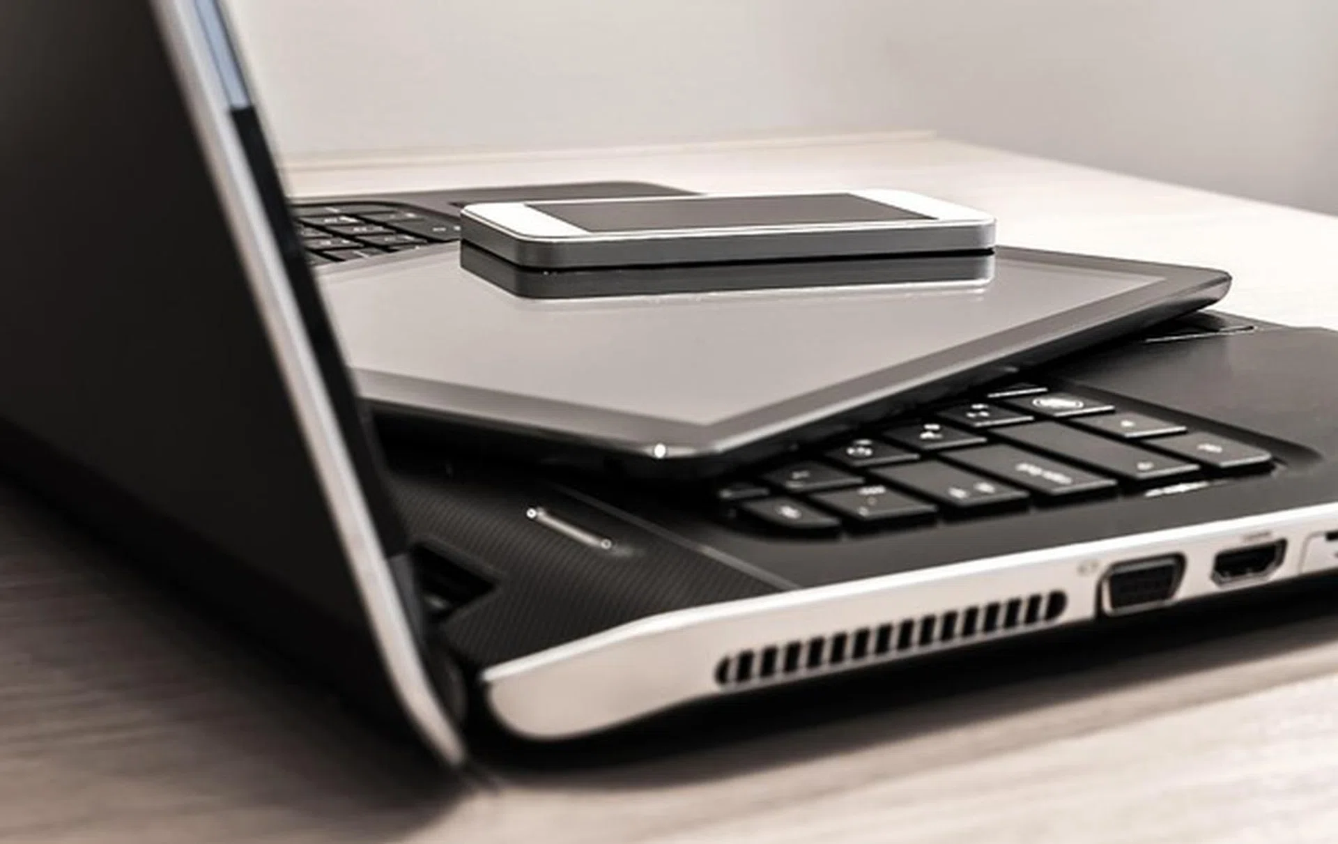 An open laptop, taken from the side. On its keyboard is a ipad and iphone