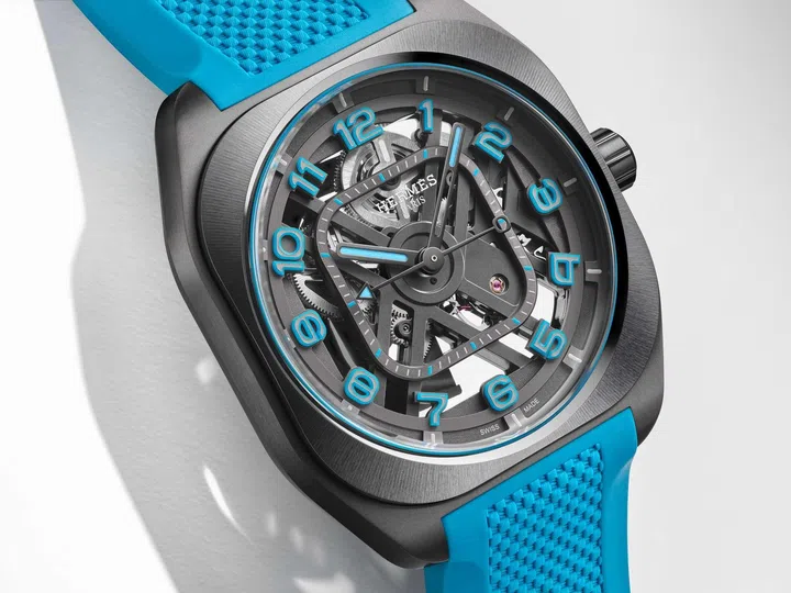 The Hermès H08 Squelette with a skeletonised automatic movement visible through an openworked dial, housed in a satin-brushed titanium case and paired with a vivid Bleu Zanzibar rubber strap accented by blue Super-LumiNova numerals and hands.