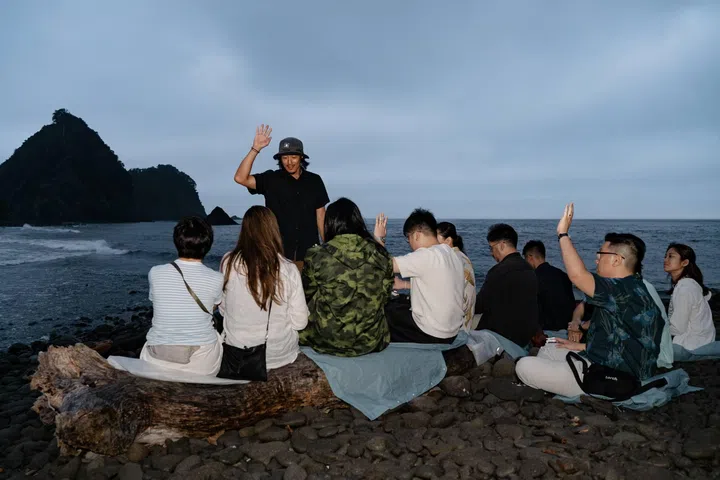 Award-winning freediving photographer Kohei Ueno leading a breathing exercise on Sebama Coast in western Izu Peninsula, with participants seated on the shoreline overlooking the Pacific Ocean as part of the Grand Seiko Ushio Journey.