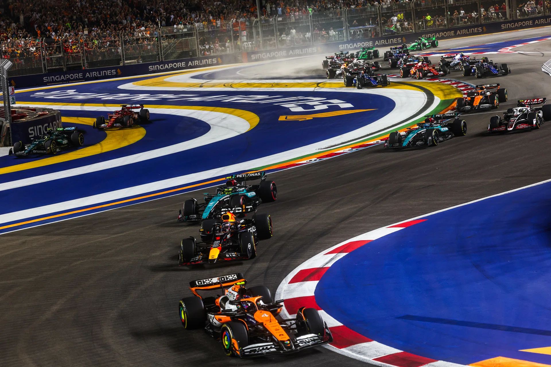 MARINA BAY STREET CIRCUIT, SINGAPORE - SEPTEMBER 22: Lando Norris, McLaren MCL38, leads Sergio Perez, Red Bull Racing RB20, Sir Lewis Hamilton, Mercedes F1 W15, George Russell, Mercedes F1 W15, and the rest of the field as Fernando Alonso, Aston Martin AMR24, and Charles Leclerc, Ferrari SF-24, cut on the opening lap during the Singapore GP at Marina Bay Street Circuit on Sunday September 22, 2024 in Singapore, Singapore. (Photo by Alastair Staley / Motorsport Images)