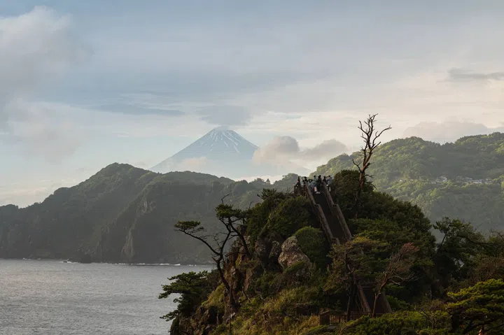 View of Mount Fuji from the western coast of Japan’s Izu Peninsula across Suruga Bay, with the snow-capped volcano rising above the horizon under a clear sky, framed by the coastal landscape of western Izu