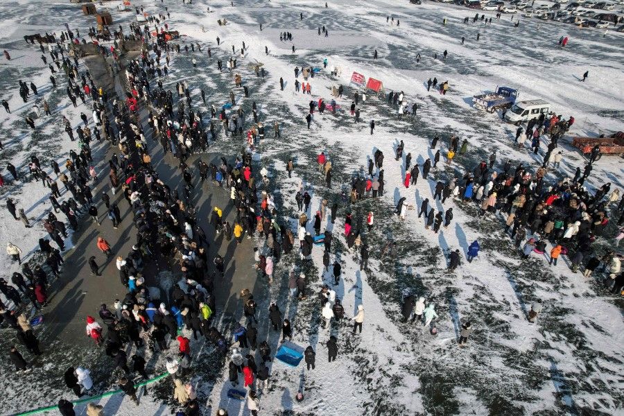 This aerial photo shows visitors watching as fishermen use a net placed under the ice to catch fish during the annual Chagan Lake Winter Fishing Festival in Songyuan, in northeast China's Jilin province on 28 December 2022. (Jade Gao/AFP)