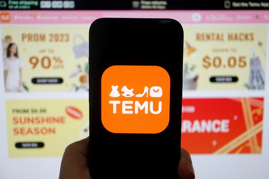 The logo of Temu, an e-commerce platform owned by PDD Holdings, is seen on a mobile phone displayed in front of its website, in this illustration picture taken 26 April 2023. (Florence Lo/Illustration/Reuters)