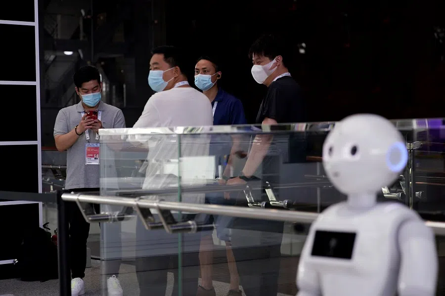 People wearing face masks stand near a robot at the venue for the World Artificial Intelligence Conference (WAIC) in Shanghai, China, 9 July 2020. (Aly Song/Reuters)