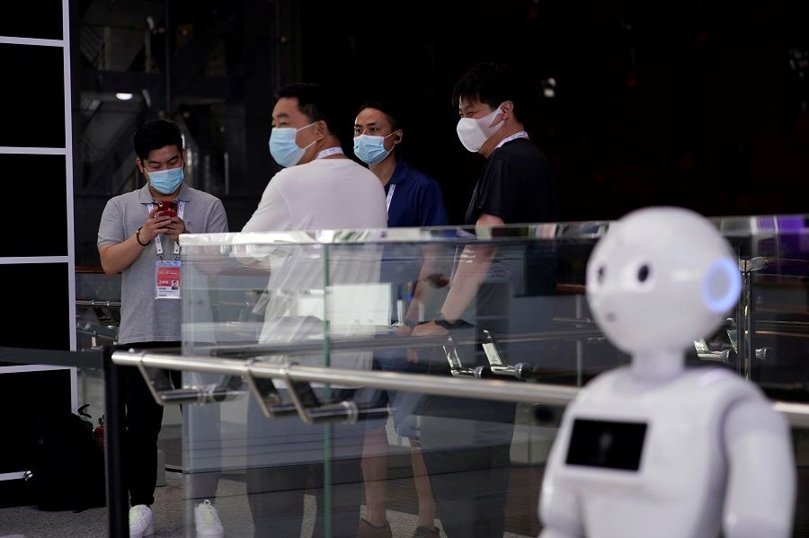 People wearing face masks stand near a robot at the venue for the World Artificial Intelligence Conference (WAIC) in Shanghai, China, 9 July 2020. (Aly Song/Reuters)