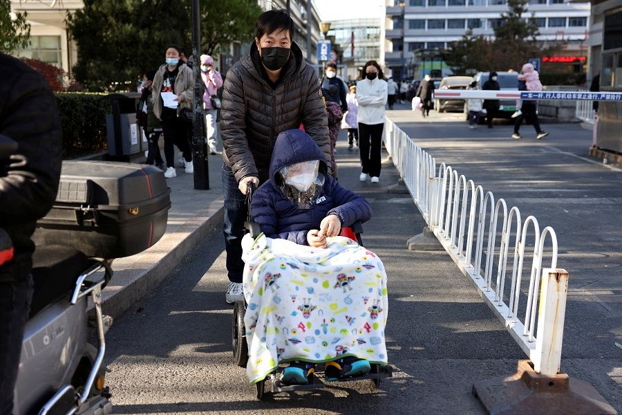 A man pushes a child covered in a blanket in a wheelchair outside a children's hospital in Beijing, China, on 24 November 2023. (Florence Lo/Reuters)