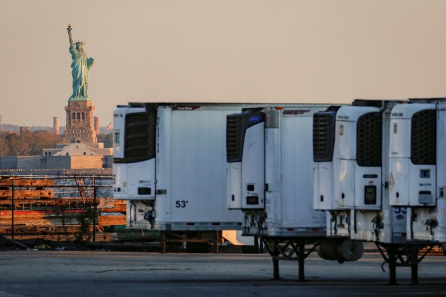 Refrigerated tractor trailers used to store bodies of deceased people are seen at a temporary morgue, with the Statue of Liberty seen in the background, during the Covid-19 outbreak, in the Brooklyn borough of New York City, US, 13 May 2020. (Brendan McDermid/Reuters)