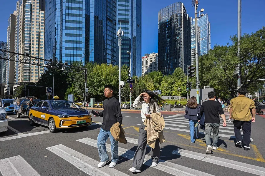 People cross a road in the business district in Beijing, China, on 8 October 2024. (Adek Berry/AFP)
