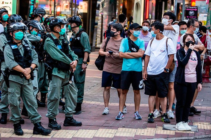 Police stand guard on a corner while pedestrians wait to cross the road during a protest against China's planned national security law in Hong Kong on 28 June 2020. (Isaac Lawrence/AFP)