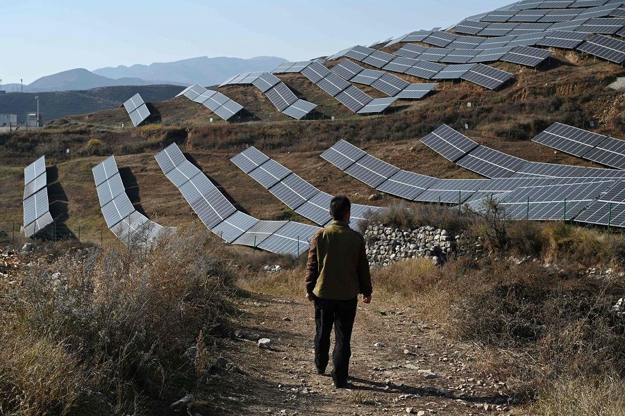 This photo taken on 23 October 2021 shows a villager walking near solar panels on a hillside at Huangjiao village in Baoding in Hebei province, China. (Greg Baker/AFP)