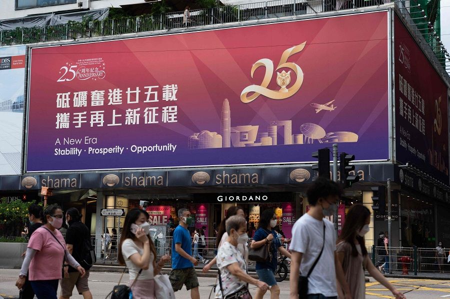 People walk past a billboard with a slogan celebrating the 25th anniversary of Hong Kong's handover from Britain to China, in the Tsim Sha Tsui district of Hong Kong on 12 June 2022. (Bertha Wang/AFP)