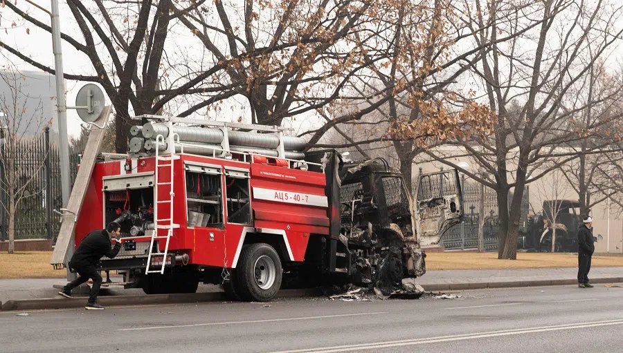 A man protects himself behind a burnt firefighter's vehicle in central Almaty, Kazakhstan, on 7 January 2022, after unprecedented unrest in the Central Asian nation due to a hike in energy prices. (Alexandr Bogdanov/AFP)
