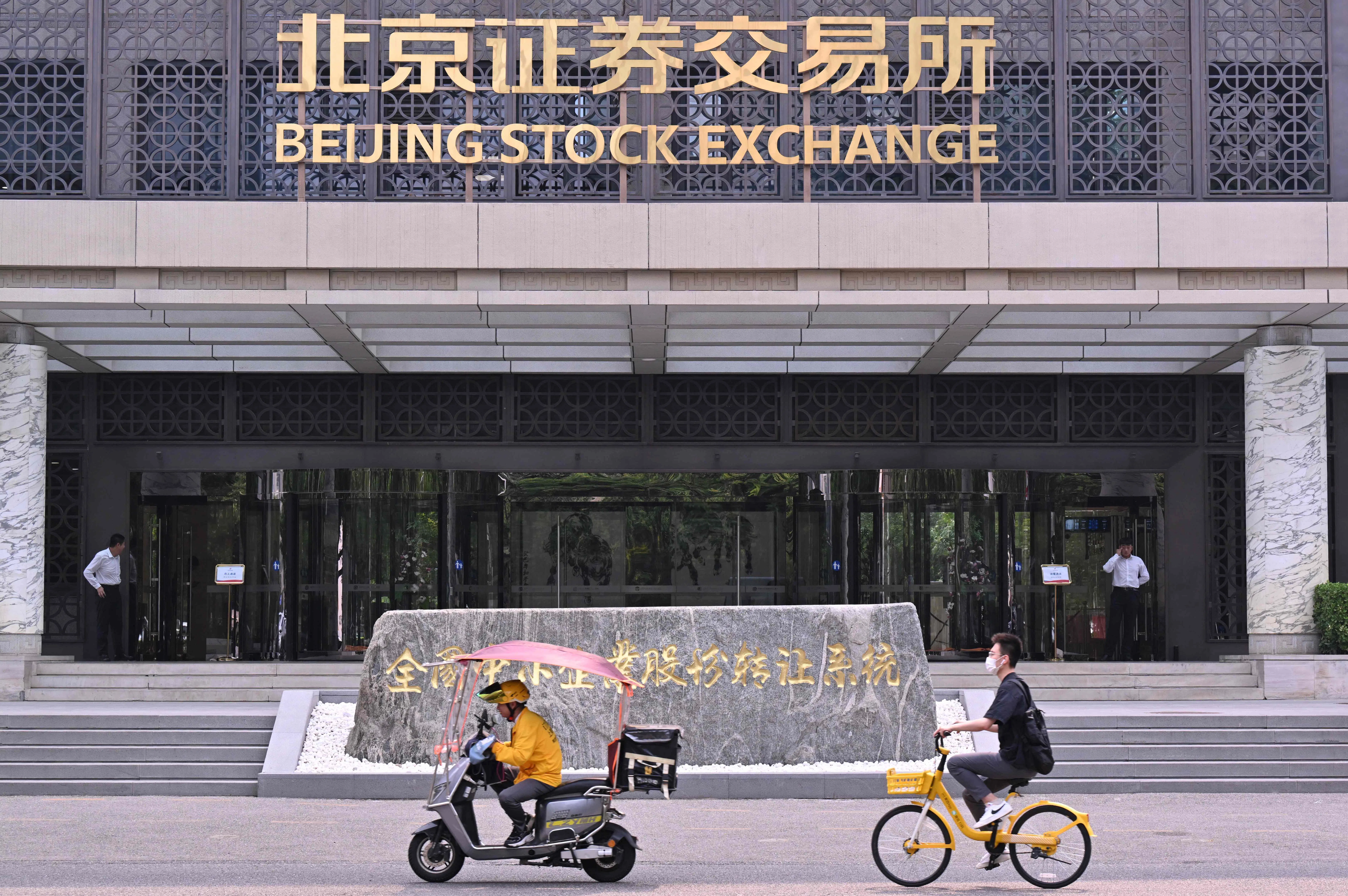 People ride vehicles past the Beijing Stock Exchange in Beijing on 9 July 2024. (Adek Berry/AFP)