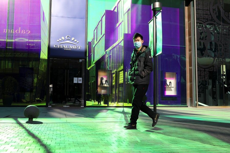A man wearing a mask to prevent the spread of Covid-19 walks past luxury fashion stores at a shopping complex in Beijing, China, 1 December 2021. (Tingshu Wang/Reuters)