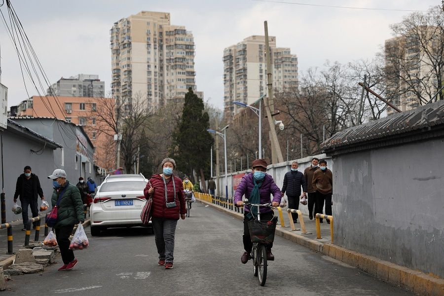 People wearing face masks to prevent the spread of Covid-19, walk past residential buildings in Beijing, China, 30 March 2022. (Tingshu Wang/Reuters)