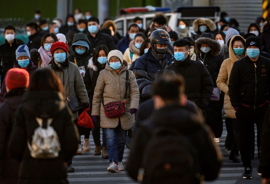 People wearing face masks walk along a street during a rush hour in Bejing on 16 December 2020. (Noel Celis/AFP)