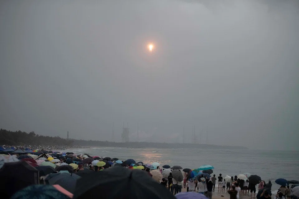 A crowd watches from a beach as a Long March 5 rocket, carrying the Chang’e-6 mission lunar probe, lifts off as it rains at the Wenchang Space Launch Centre in southern China’s Hainan Province on 3 May 2024. (AFP)