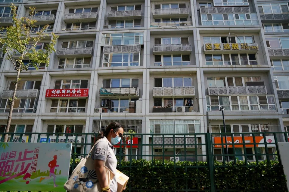 A woman wearing a face mask following the coronavirus disease (COVID-19) outbreak walks past a residential compound in Beijing, China, 11 August 2020. (Tingshu Wang/REUTERS)