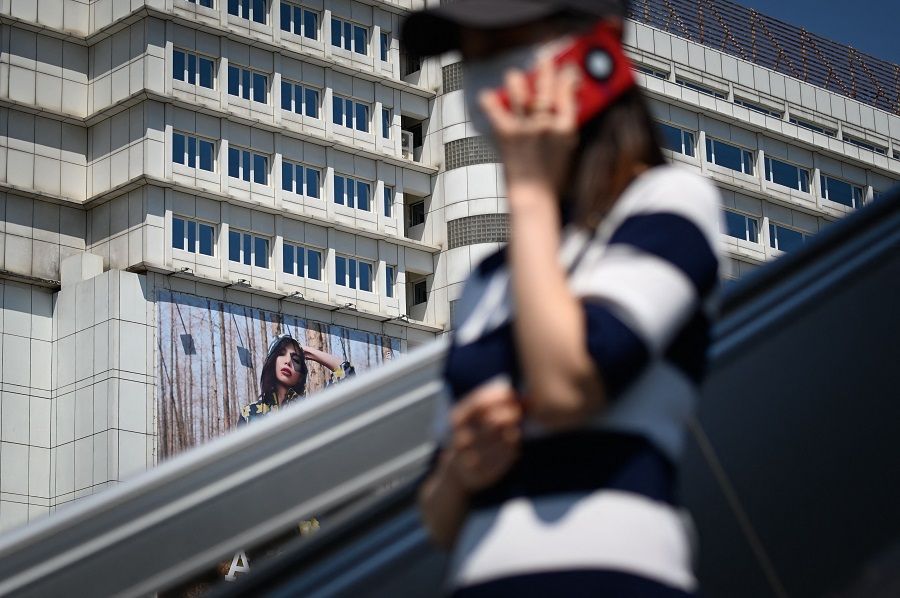 A woman uses her mobile phone as she rides an escalator past an advertising board at a business district in Beijing, China, on 16 May 2022. (Wang Zhao/AFP)
