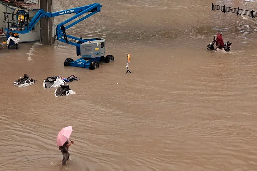 This photo taken on 20 July 2021 shows people wading through flood waters along a street following heavy rains in Zhengzhou, Henan province, China. (STR/AFP)